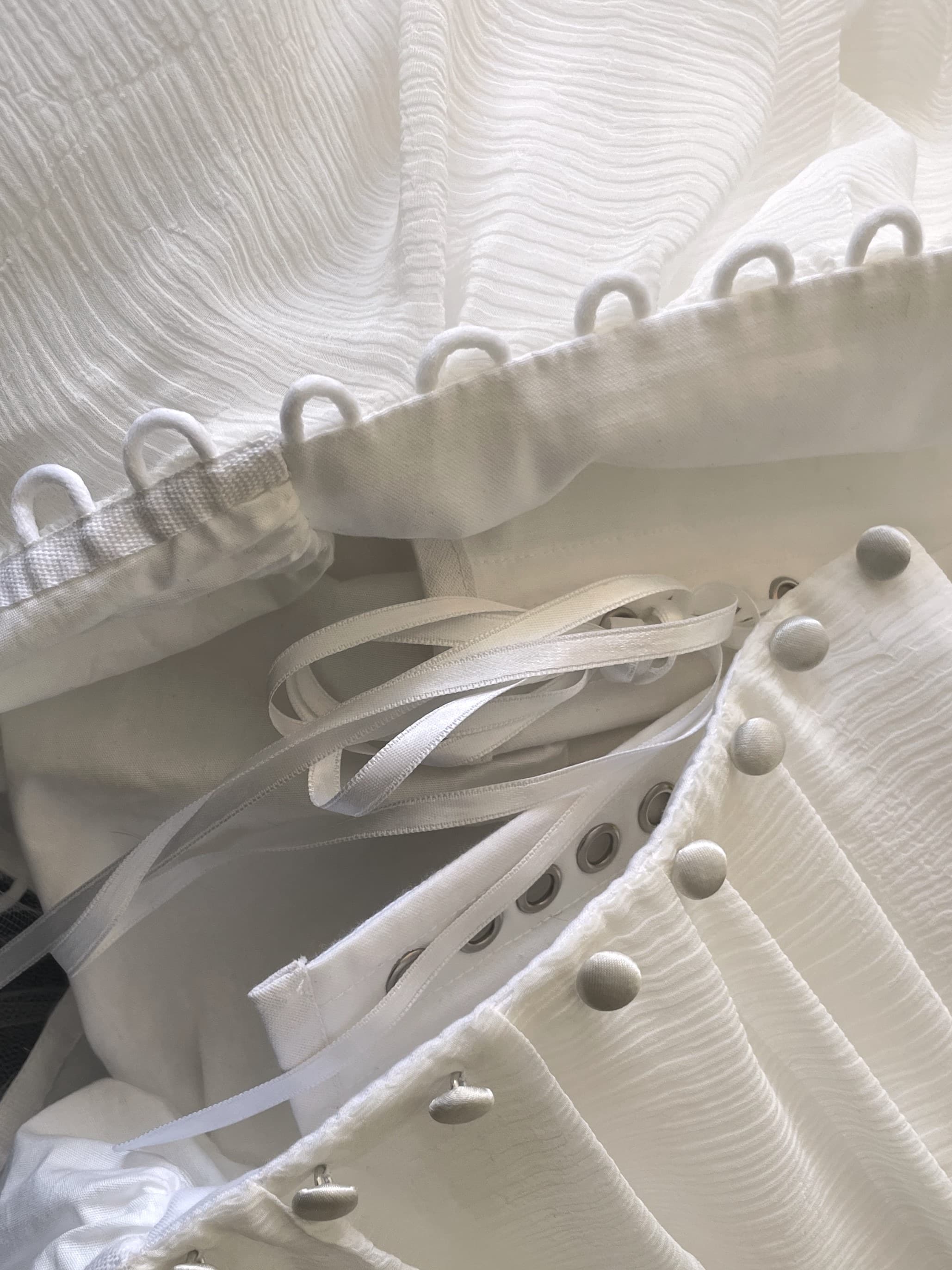 Détail d'un dos de robe : boutons recouverts, œillets et rubans de laçage